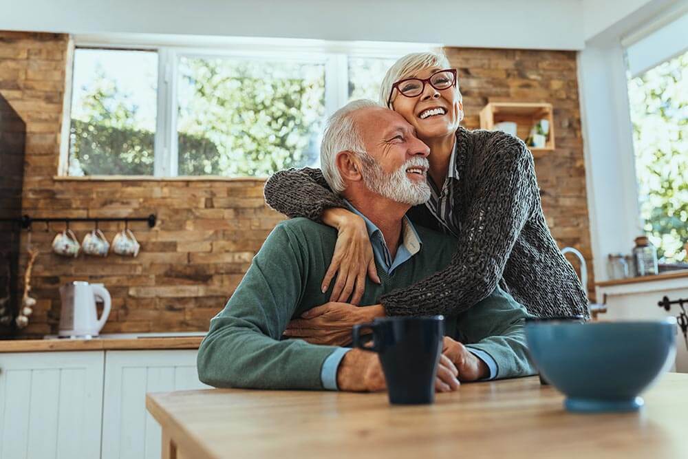 Smiling older man and woman embracing in kitchen 